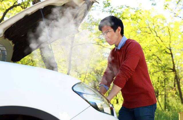 Man looking at smoking car engine